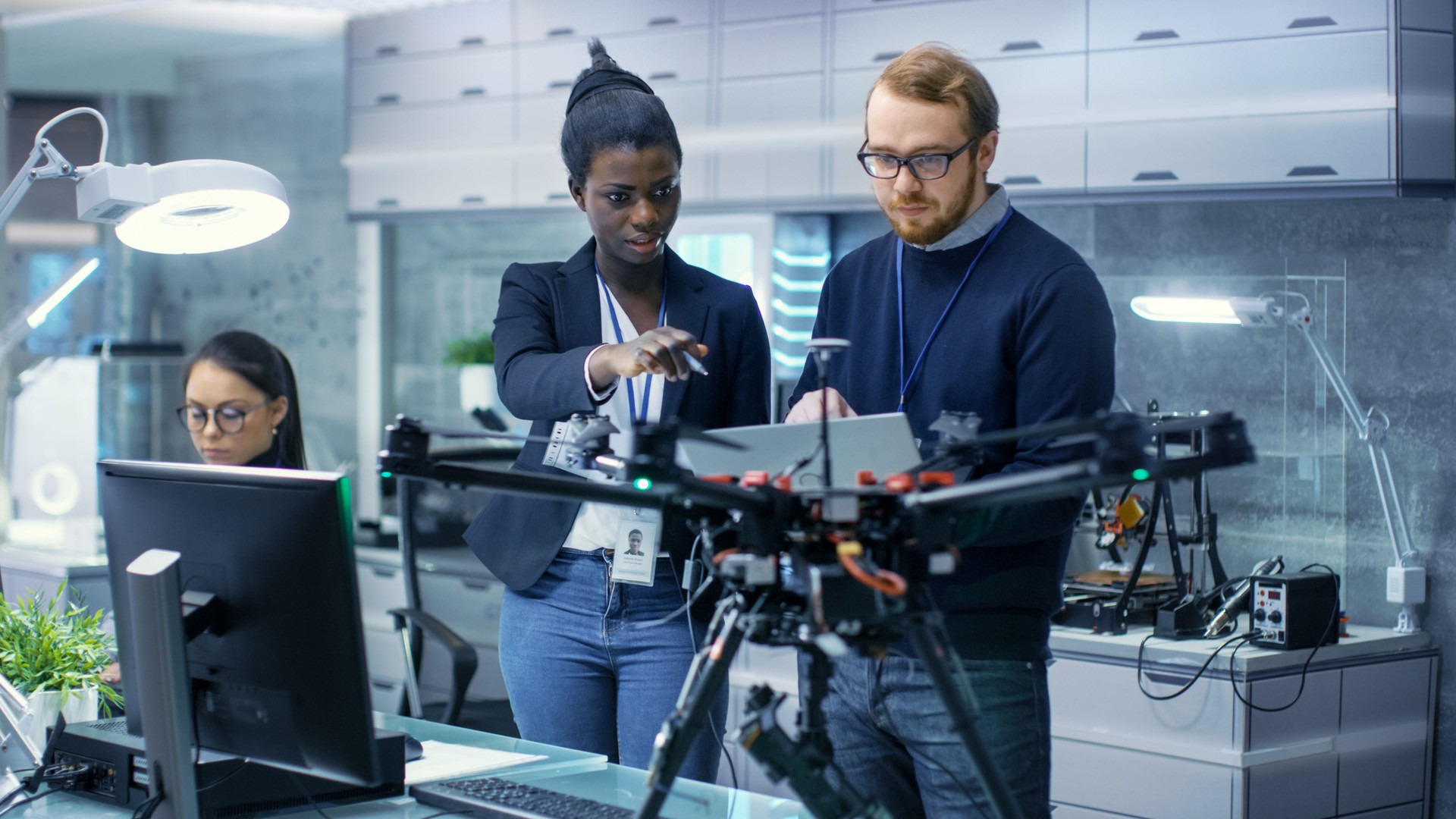 Ingegneri maschi e neri caucasici che lavorano a un progetto drone con l'aiuto di laptop e prendere appunti. Lavora in un laboratorio high-tech moderno brillante.